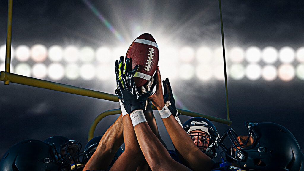 Football players reaching for the ball under stadium lights, representing Patrick Mahomes and NFL performance.